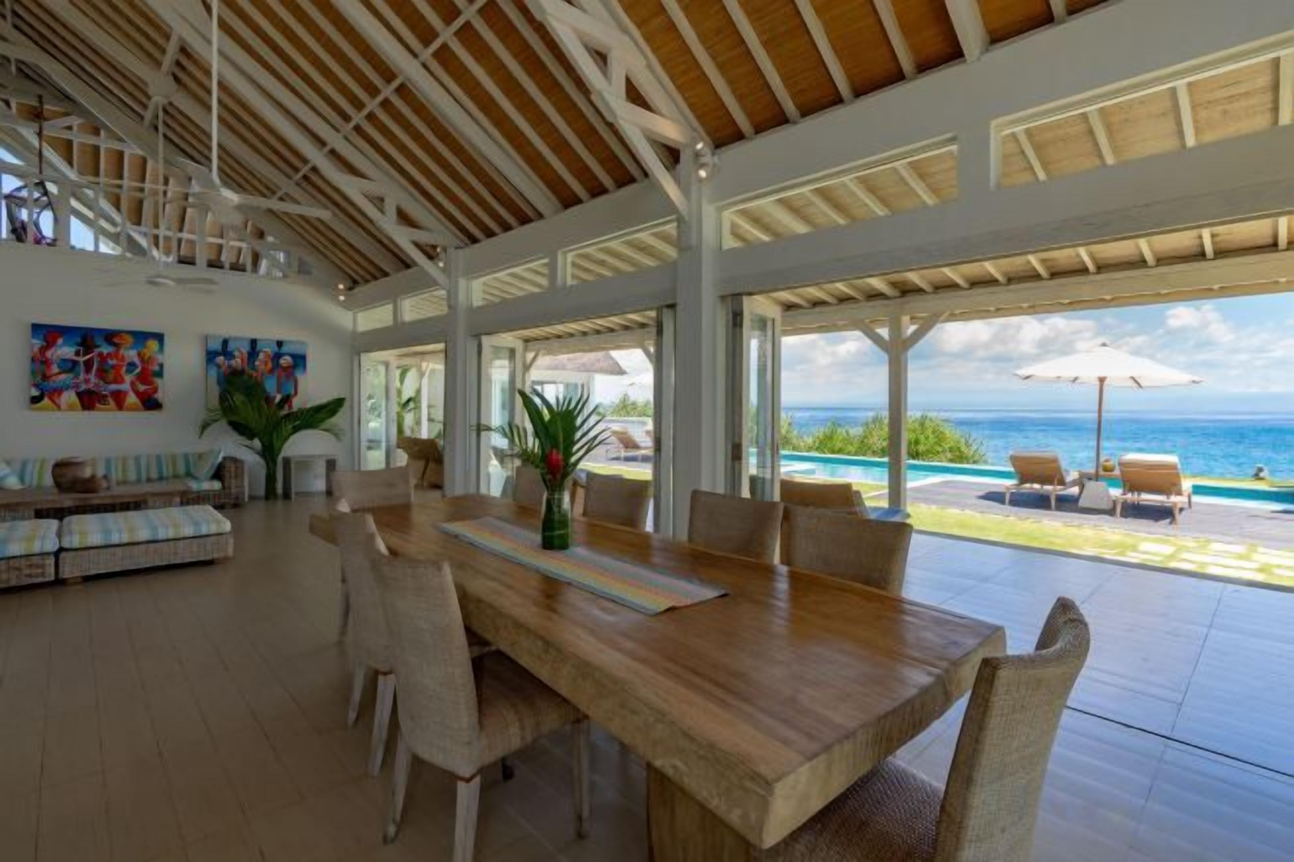 An open-plan living area with a wooden dining table, chairs, and a view of the ocean.