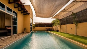 Una piscina con un porche techado, puerta corrediza de vidrio y una pequeña zona de estar al aire libre.