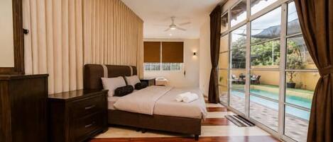 A bedroom with a bed, dresser, and large windows overlooking a pool.