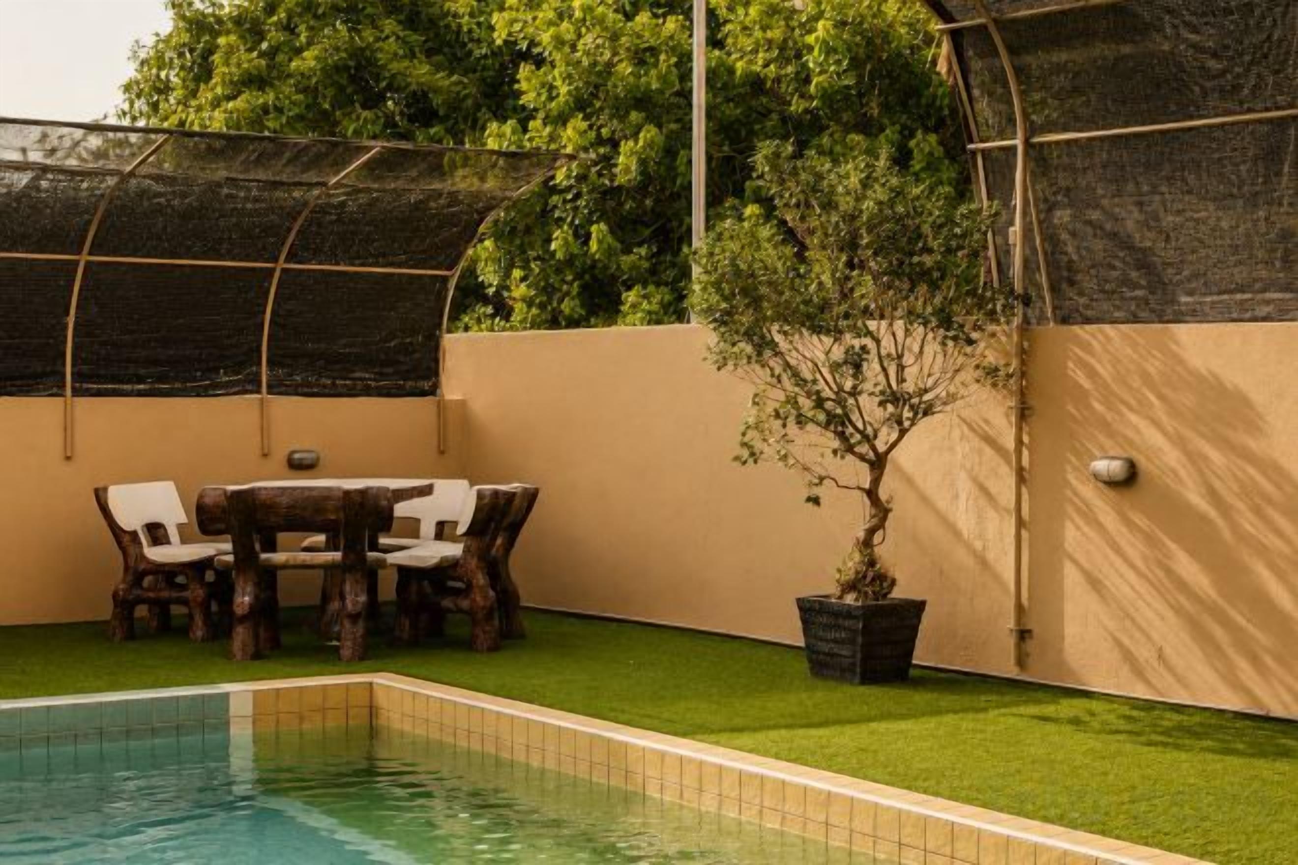 A swimming pool with a table and chairs, surrounded by a wall and a tree.