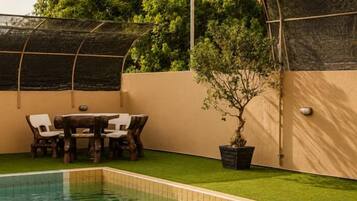 A swimming pool with a table and chairs, surrounded by a wall and a tree.