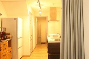 A narrow hallway with a kitchen area on the right, featuring a refrigerator, cabinets, and a sink.
