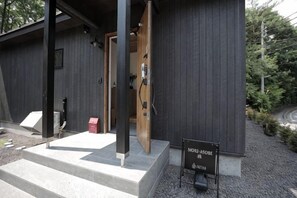 A modern building with a wooden door, a signboard, and a gravel path leading to a bench. - [TV] Luxury adult secret base villa 120 ㎡ Sauna, stone bath, bonfire, BBQ [Zen Building] (Miyota)