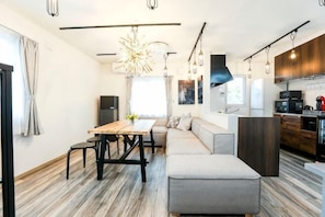 A modern kitchen with a dining area, a sofa, and a large window.