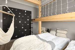 Una cama litera con hamaca, una pared negra con diseños recortados y una colcha gris y blanca.