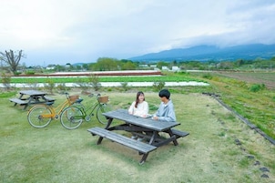 Dos personas sentadas en una mesa de picnic en un entorno al aire libre, con bicicletas y un campo de césped al fondo.