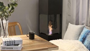 Et hyggeligt rum med pejs, et træbord med bøger og en kop, samt en behagelig sofa.