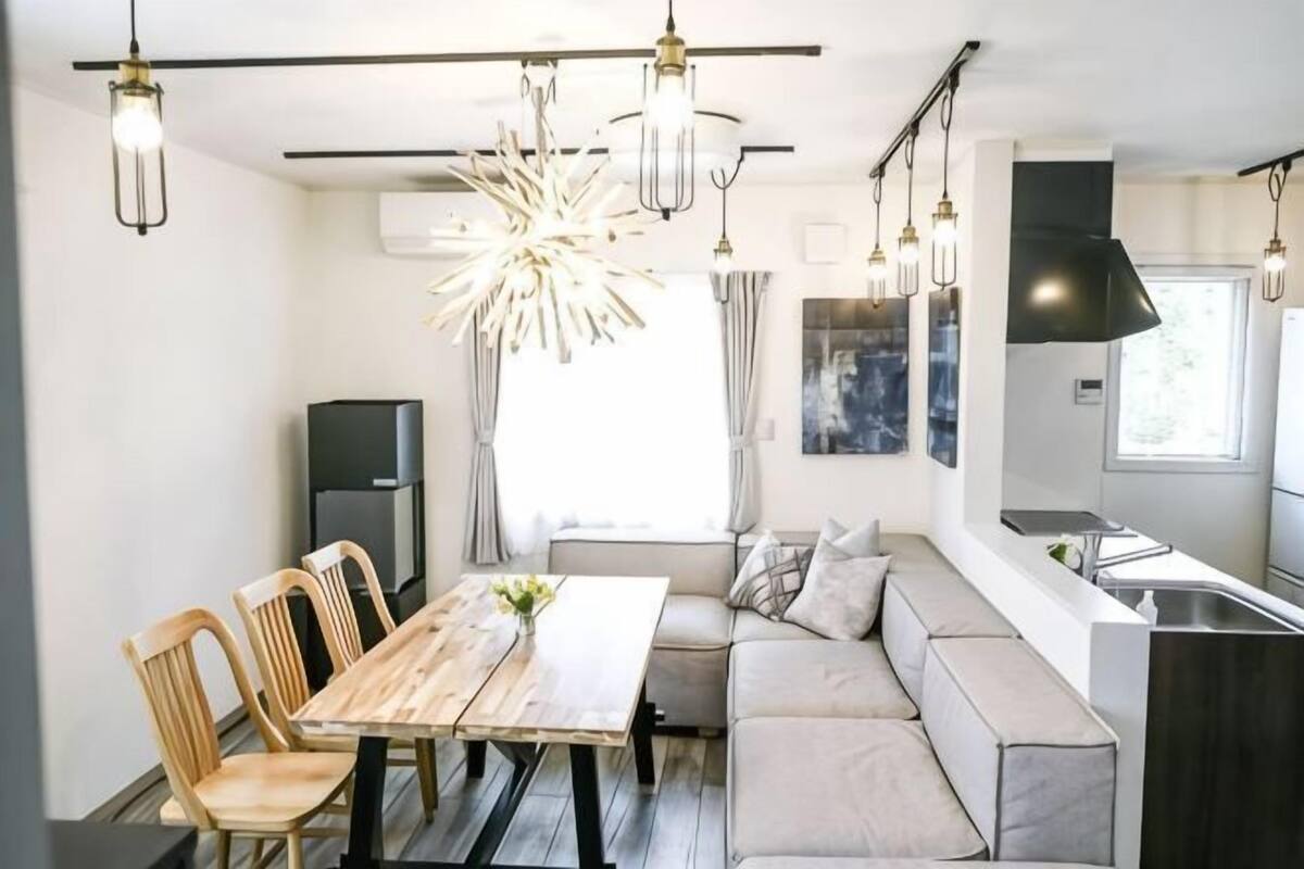 Une cuisine moderne dotée d’un four encastré, un coin repas avec une table et des chaises en bois, et un espace détente avec des coussins.