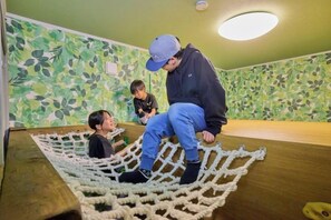Une pièce avec un plancher en bois, un filet en corde et un mur recouvert de plantes vertes.