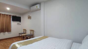 A hotel room with a bed, a desk, two chairs, an air conditioning unit, and a window with curtains.