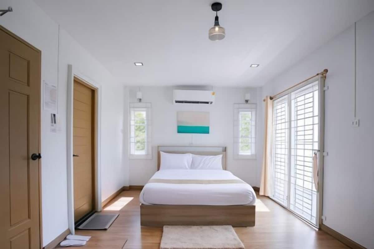 A bedroom with a bed, a window, a door, and a ceiling light.