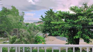 A balcony with a white railing, overlooking a garden with various trees and a clear sky.