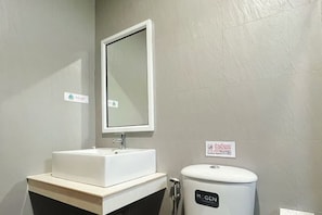 Ein Badezimmer mit einem weißen Waschbecken, einem Spiegel und einer Toilette mit der Aufschrift 'MOGEN'.