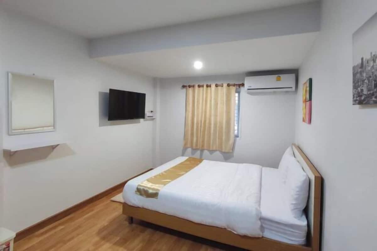 A bedroom with a bed, a television, an air conditioner, a window with curtains, and a wall-mounted picture.