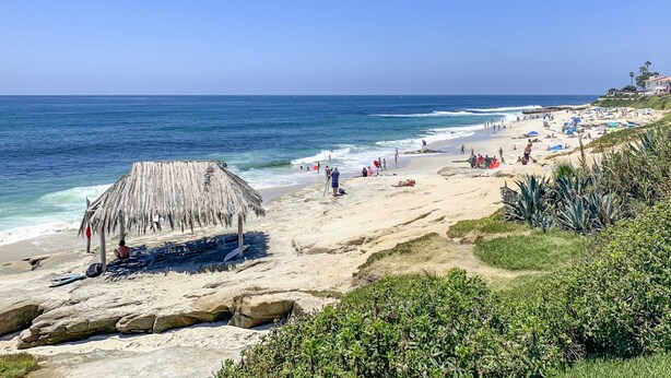 Una playa con una cabaña de techo de paja, terreno rocoso y una vista despejada del océano.