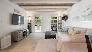 Un salón amplio con techo de madera, un televisor de pantalla plana grande, un sofá color beige y una mesa de centro.