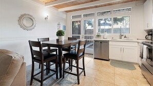 Una cocina moderna con armarios blancos, techo de madera y comedor con mesa y sillas.