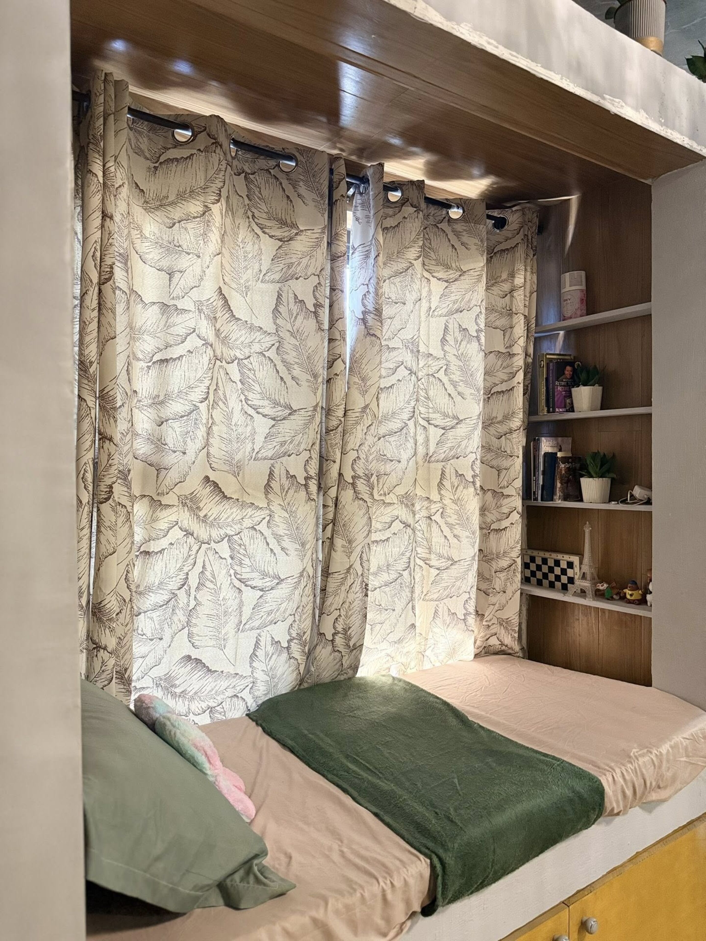 Un letto a castello con coperta verde e trapunto beige. Si vede uno scaffale con libri e una piccola riproduzione della Torre Eiffel.