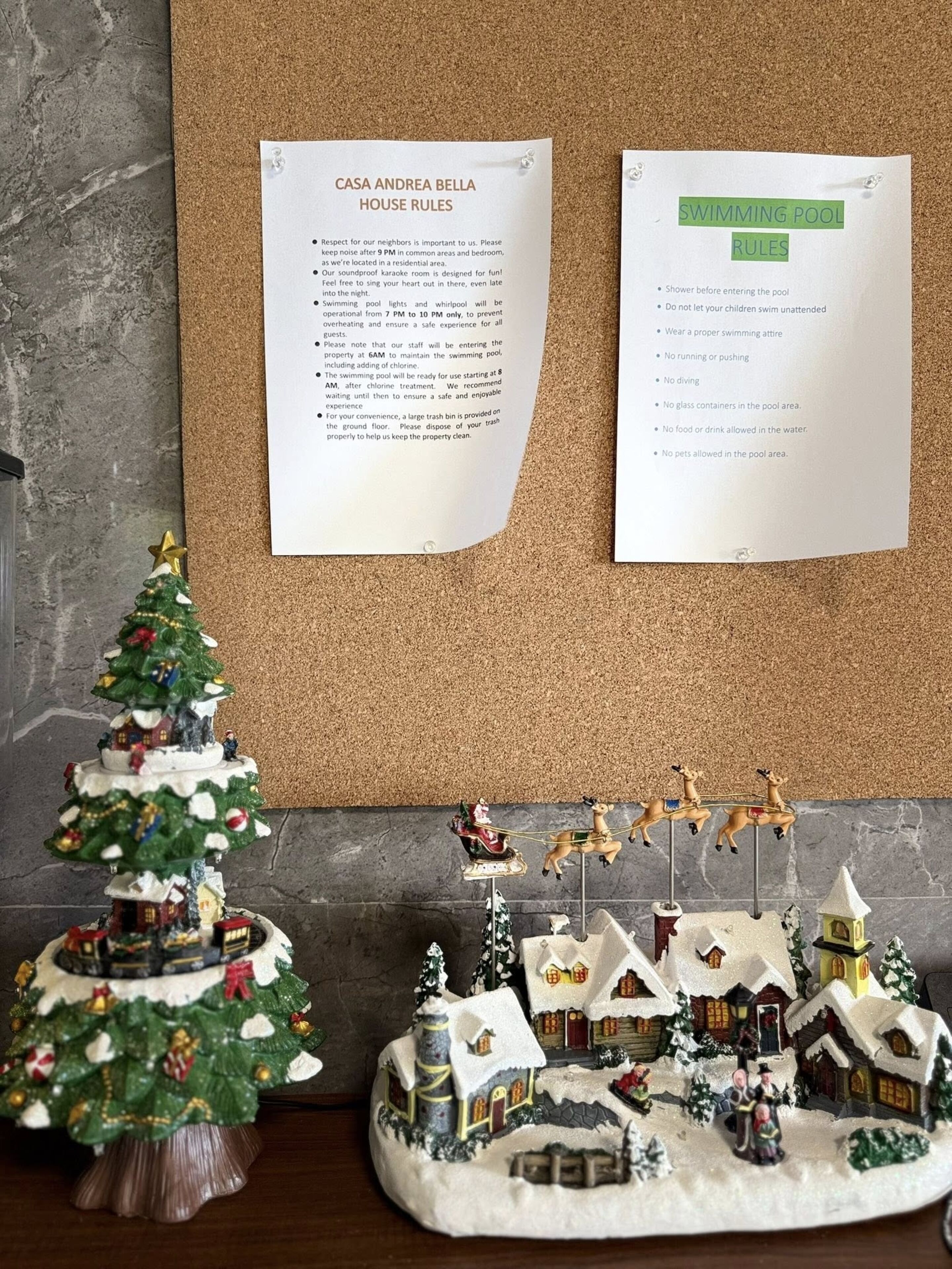 Eine Korktafel mit zwei Hinweisschildern: 'Casa Andrea Bella Hausordnung' und 'Schwimmbadregeln'.