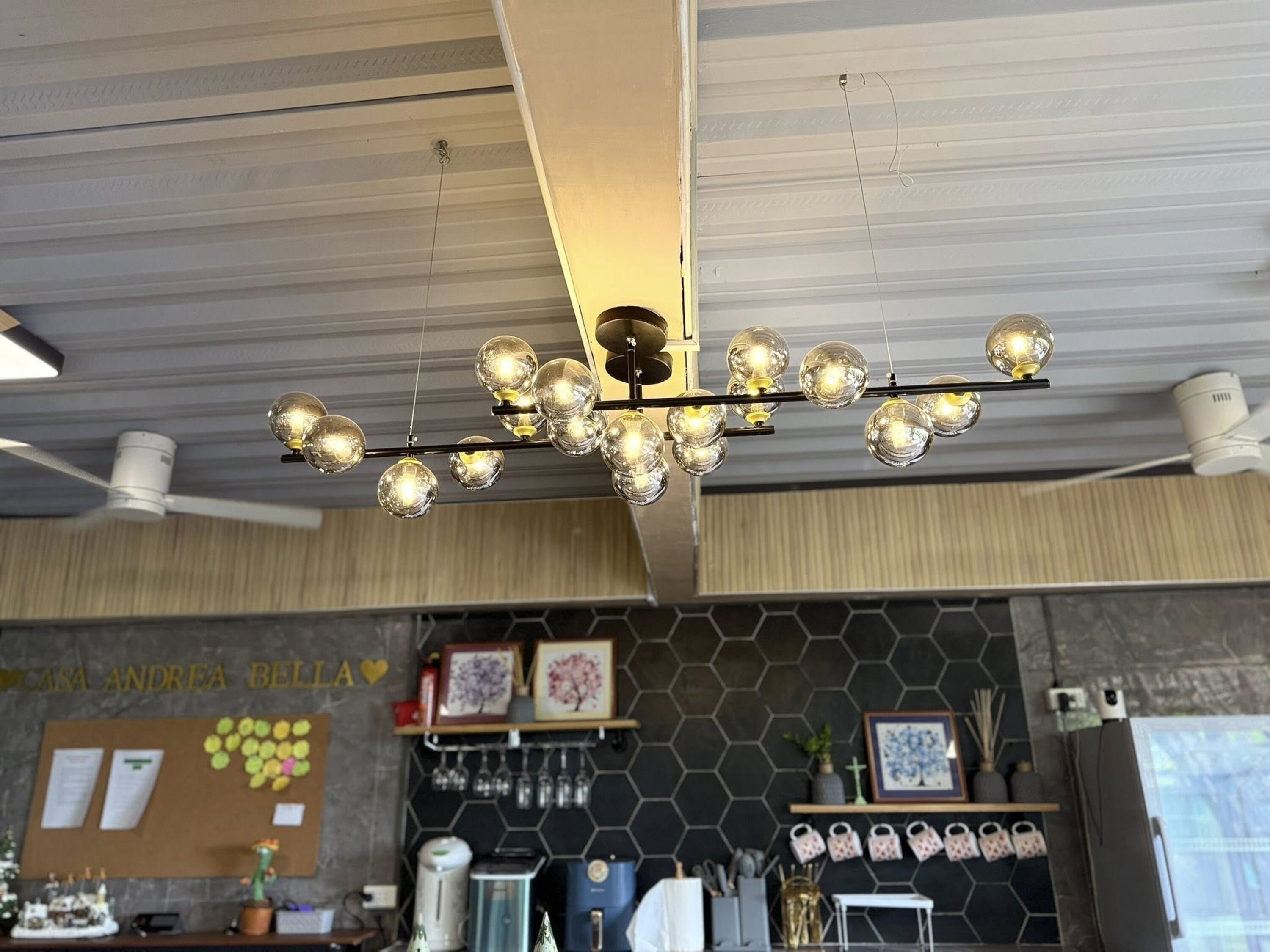 A modern kitchen with a hexagonal tile backsplash, a ceiling fan, and a chandelier with multiple spherical lights.
