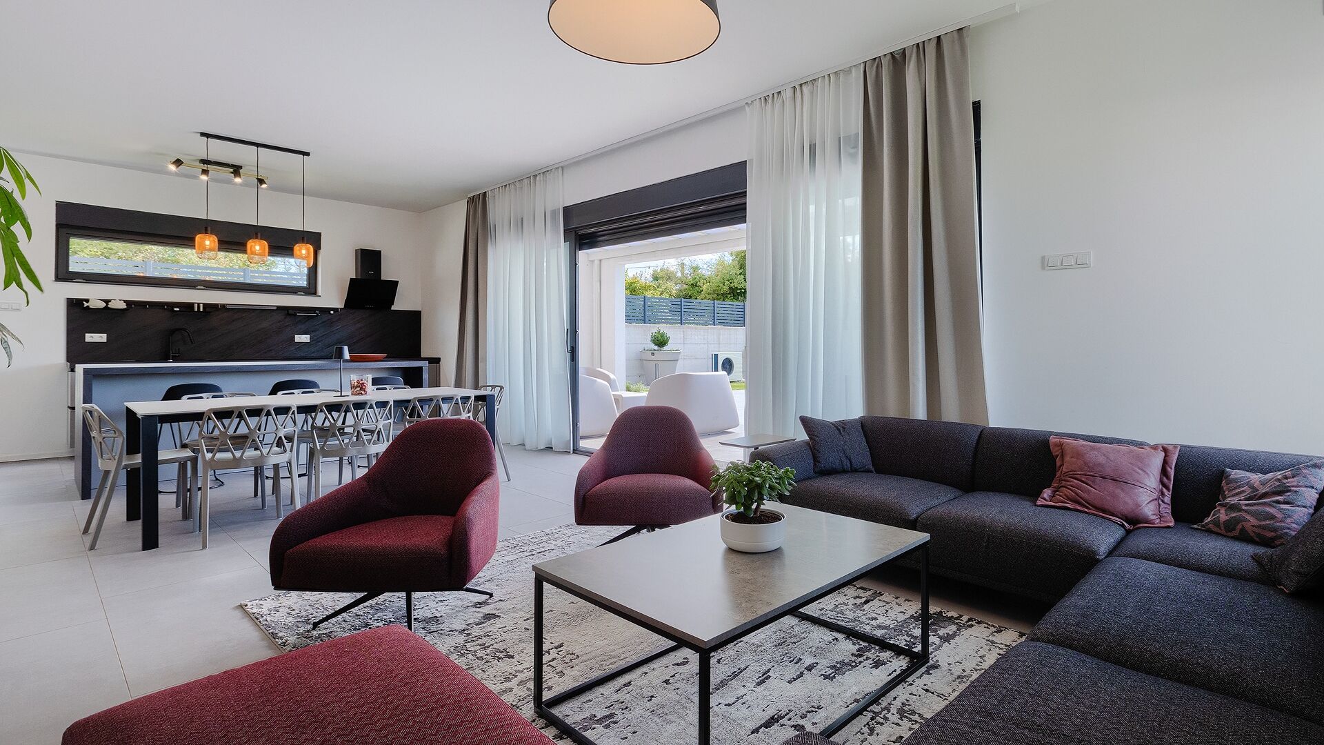 Una sala de estar moderna con un sofá, sillas, una mesa baja y una zona de comedor con mesa y sillas.