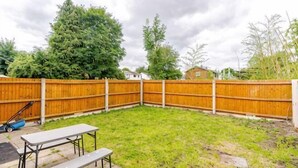 Een achtertuin met houten omheining, een picknicktafel en een bank.