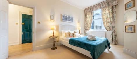 A bedroom with a bed, bedside lamps, a window with curtains, and a door leading to another room.