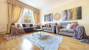 A living room with a sofa, armchairs, a coffee table, and a rug. There are curtains, a window, and artwork on the wall. - South Kensington - Cromwell Rd Residence (London)