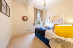 A bedroom with a bed, a window with curtains, a chandelier, a bedside table, and a lamp. - South Kensington - Cromwell Rd Residence (London)