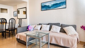 A living room with a sofa, a glass coffee table, a dining area with chairs, and a framed picture on the wall.