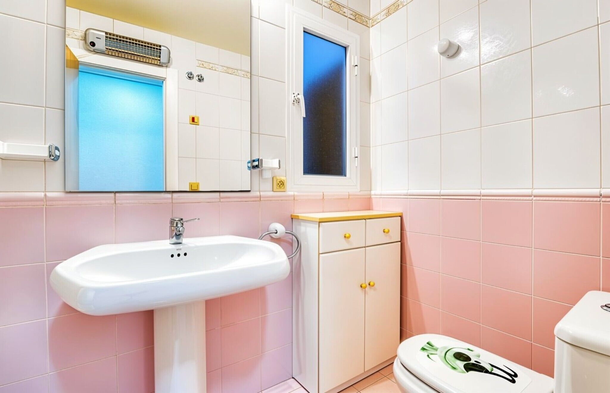 A bathroom with a white sink, a mirror, a window, and a toilet.