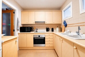 Una cocina compacta con armarios de madera, horno empotrado, microondas y un lavabo.