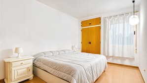 A bedroom with a bed, a nightstand, a wooden wardrobe, and a window with curtains.