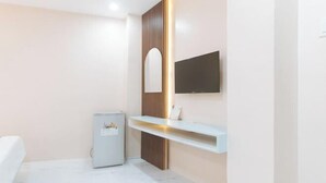 A modern bathroom with a built-in toilet, a mirror, a TV mounted on the wall, and a small shelf. - RedDoorz @ Happy Stay Apartelle (Dauis)