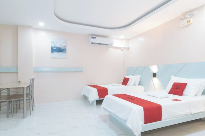 Habitación de hotel con dos camas, una mesa de comedor, sillas y un equipo de aire acondicionado.