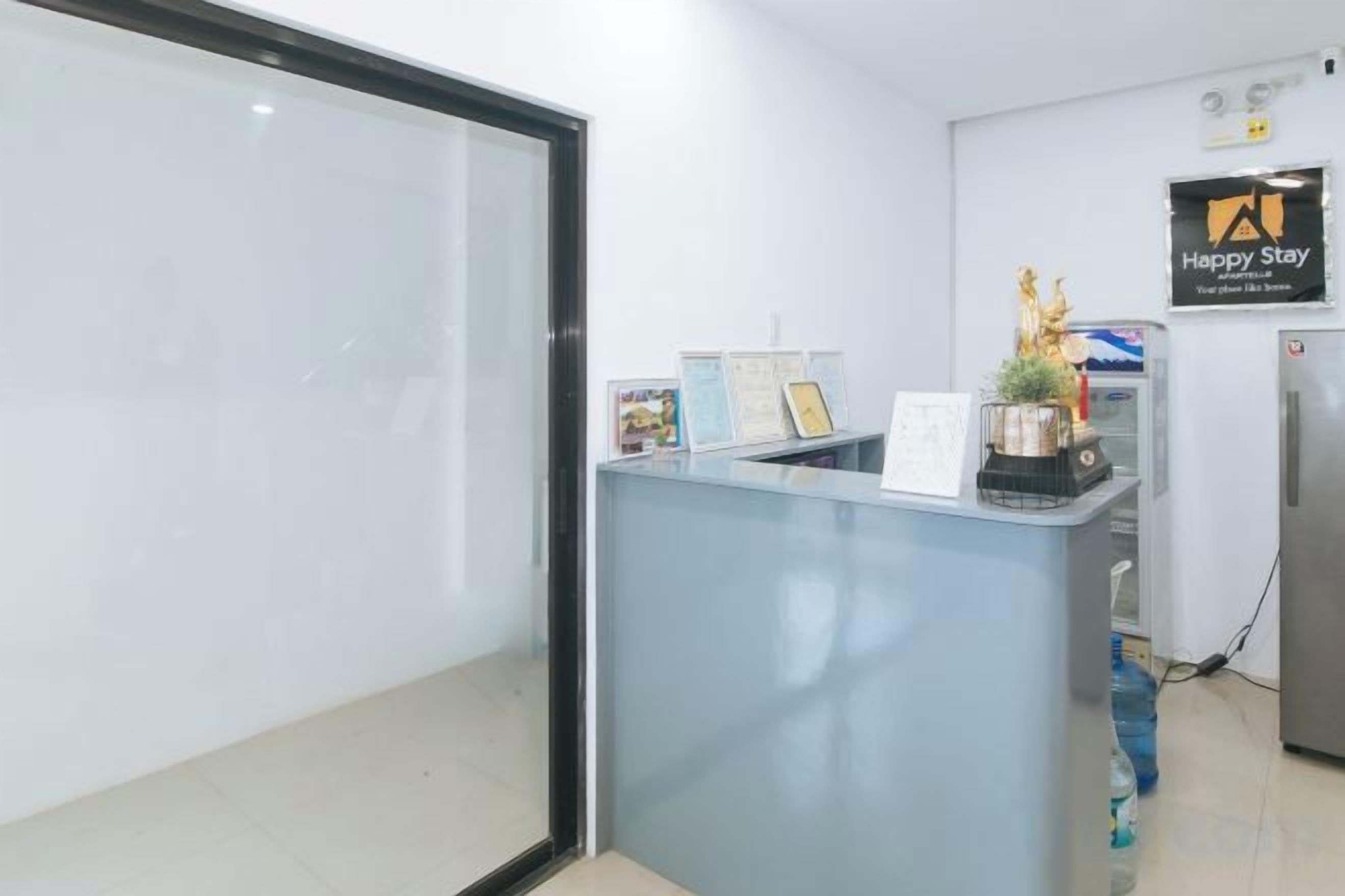 Un mostrador de recepción con separador de vidrio, un letrero que dice 'Happy Stay' y un dispensador de agua.