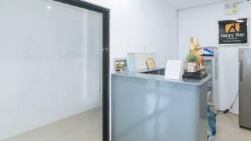 Un mostrador de recepción con separador de vidrio, un letrero que dice 'Happy Stay' y un dispensador de agua.