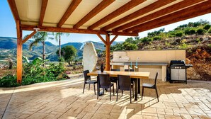 An outdoor patio with a wooden pergola, a stone table, and chairs, a barbecue grill, and a view of the surrounding landscape. - Beautiful private villa for 10 people with A/C, WIFI, pool, TV and panoramic view (Scopello)