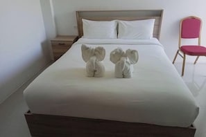 Een opgemaakt bed met witte lakens, een houten hoofdbord, een klein nachtkastje en een rode stoel.