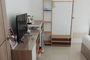 Une pièce comprenant un lit, un bureau avec un ordinateur, une télévision et une étagère avec des bouteilles.