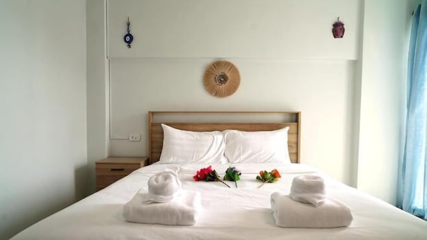Un lit bien fait, avec du linge de lit et des serviettes blanches, une tête de lit en bois, une assiette décorative accrochée au mur et une fenêtre avec des rideaux.