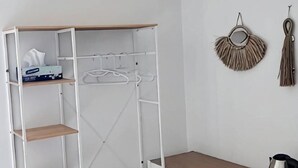 Une armoire en métal blanc, dotée d’étagères et d’un espace pour suspendre des vêtements, une table en bois et un objet décoratif fixé au mur.