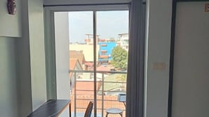 Une pièce dotée d’une grande porte-fenêtre coulissante donnant sur un balcon. Le balcon est muni d’une rambarde en métal et d’une petite table avec une chaise.