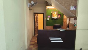 A reception area with a checkered floor, a reception desk, a green wall with a framed picture, and a staircase. - Balaji Lodging  (Hinjawadi)