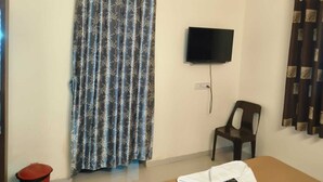 A room with a curtain, a television mounted on the wall, a chair, and a small trash bin. - Balaji Lodging  (Hinjawadi)