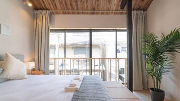 A hotel room with a bed, a potted plant, a balcony with a view, and a wooden ceiling.