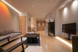 A modern living room with a sofa, coffee table, TV, and kitchen area with a refrigerator and microwave. - Tabi・Stay KOHAMA｜Direct train access to popular shopping areas such as Tennoji Park (Osaka)