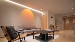 A modern living room with a sofa, a coffee table, and a chair. There is a wooden door and a staircase in the background. - Tabi・Stay KOHAMA｜Direct train access to popular shopping areas such as Tennoji Park (Osaka)