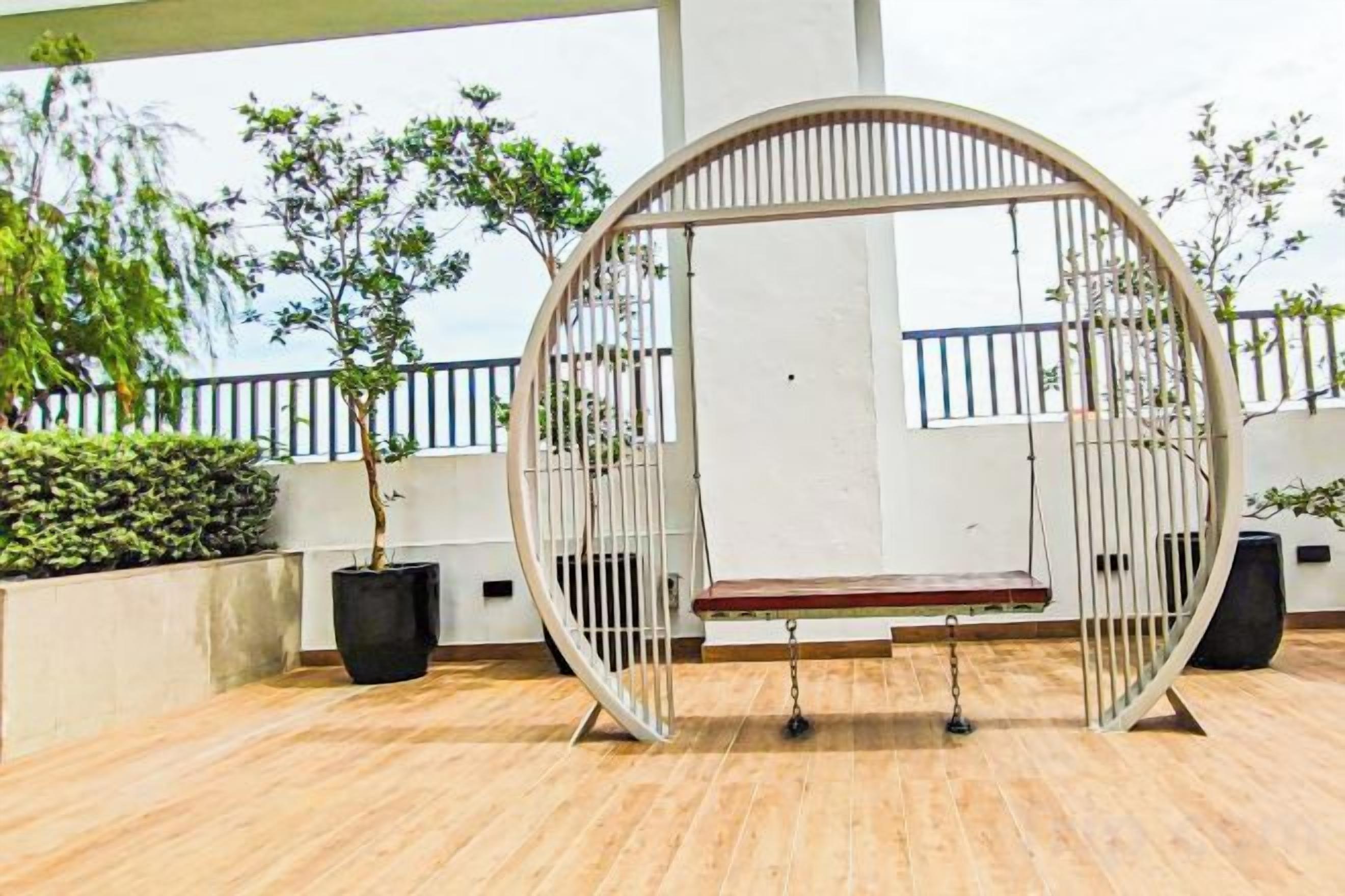 A circular swing chair with a bench, surrounded by potted plants and a railing.