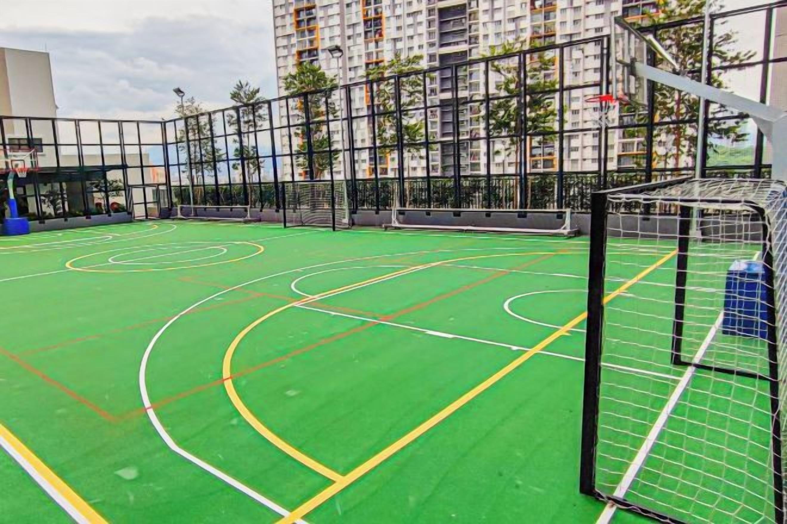 An outdoor basketball court with multiple hoops, surrounded by a fence, and adjacent to a high-rise building.